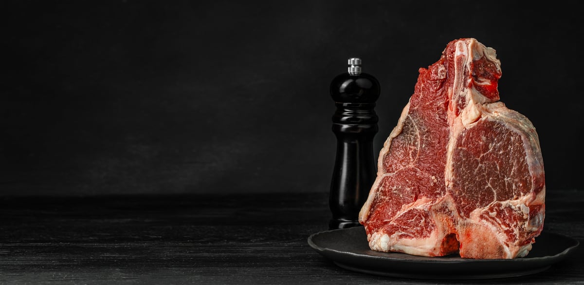 A marbled porterhouse steak presented with a pepper grinder