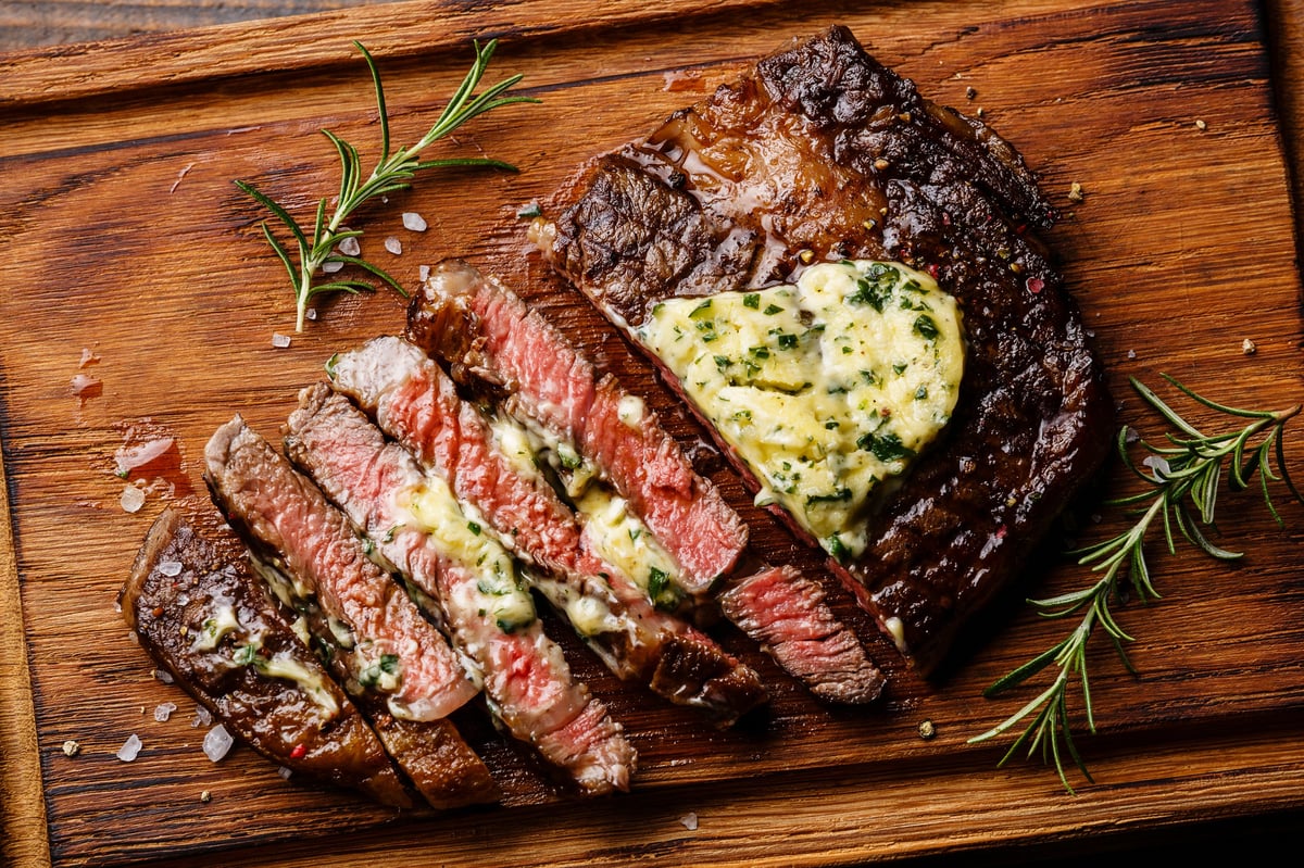 Sliced medium-rare ribeye steak with herb butter on a cutting board